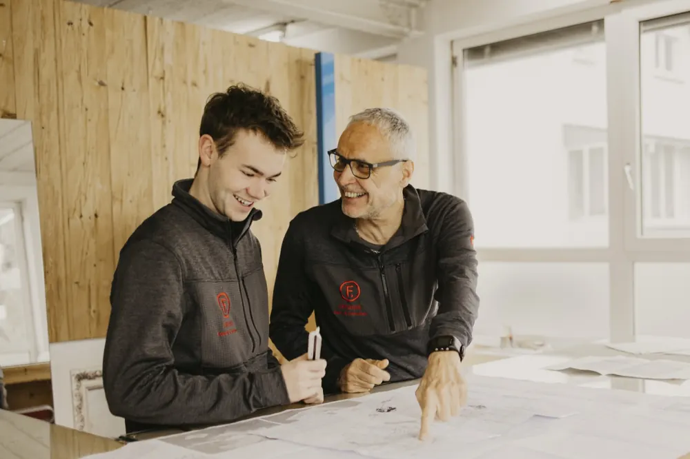 Zwei aus dem Team planen lachend einen Messestand am Tisch