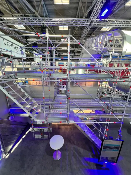 Blick von oben in den zweistöckigen Messestand von Layher aus Gerüstteilen, blau beleuchtet