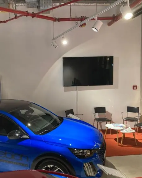 Im Showroom: blaues Auto, Bildschirm und Sitzgruppe