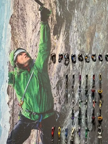 Warenwand mit Kletterausrüstung vor dem Großbild eines Eiskletterers