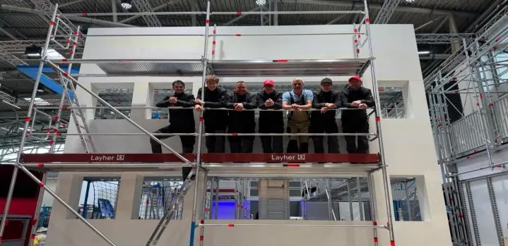 Sieben Kollegen stehen auf dem Gerüst eines Layher-Stands im Aufbau