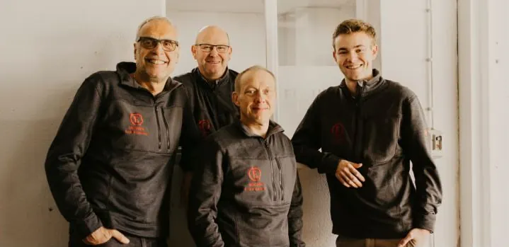 Vier aus dem Team von FREUNDE Messebau lehnen lachend an einer Wand