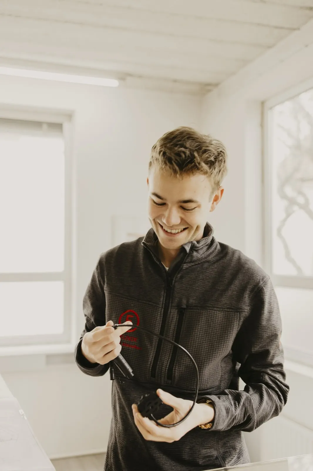 Ein Kollege hält lächelnd einen VISPAL-Sensor mit Kabel in der Hand