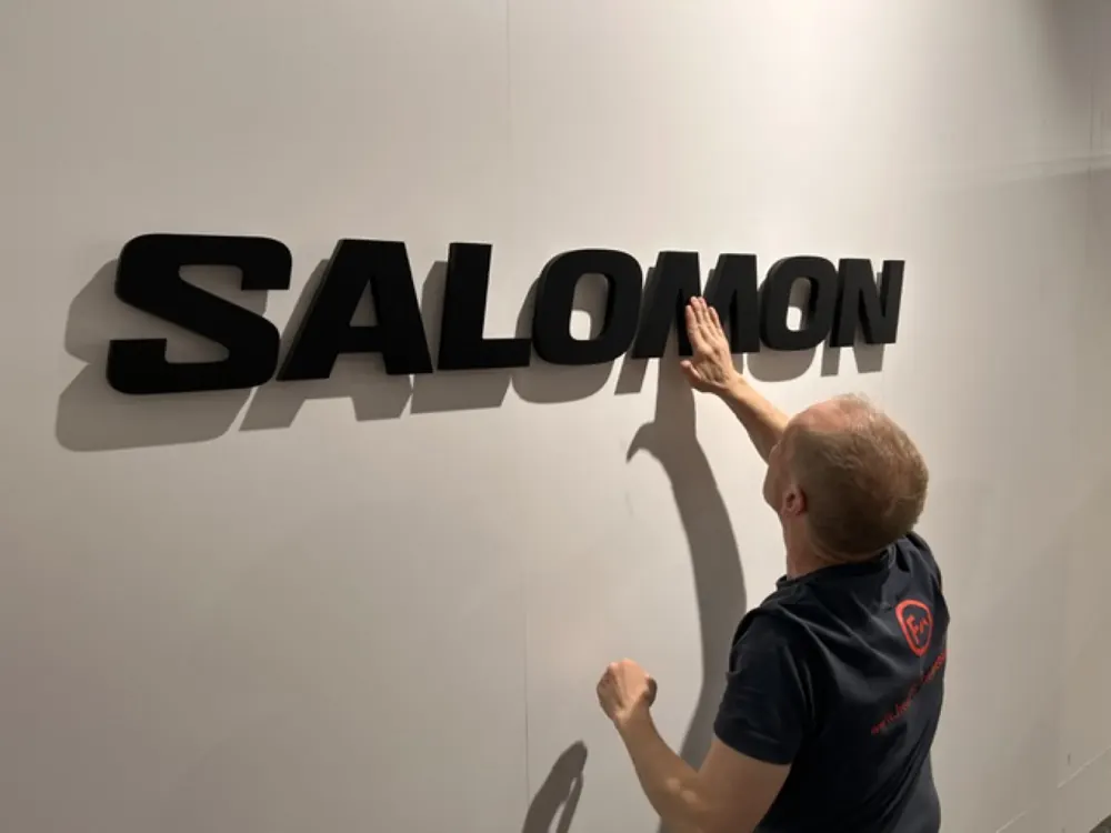 A fitter applying the Salomon lettering to a white wall